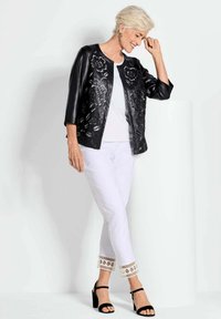 Zwarte leren jas met bloemenuitsnijdingen, witte top, witte broek met patroon aan de manchetten en zwarte hoge hakken. Eenvoudig ontwerp en contrasterende kleuren.