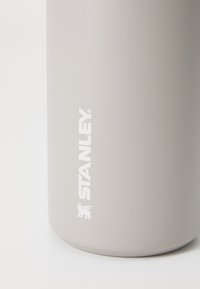 Tazza in acciaio inossidabile grigia con finitura opaca e logo bianco in rilievo. Texture liscia, forma arrotondata e base ampia.