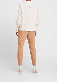 Elfenbensfärgad blus med samlade ärmar, detalj med nyckelhål i ryggen och beige skräddarsydda byxor, avslutade med blanka vita klackar. Slät tyger.