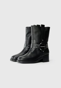 Botas de tobillo de cuero negro con un acabado texturizado, que cuentan con una correa ancha con herrajes metálicos y un tacón cuadrado.