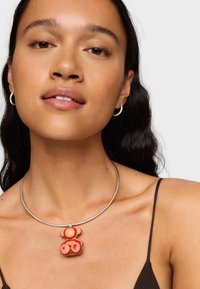 Ciondolo colorato a forma di orso in tonalità rosa su una collana d'argento, texture liscia, design circolare, indossato con una canotta scura.