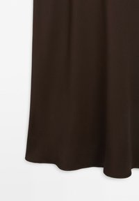 Tessuto marrone scuro con pieghe morbide appeso su uno sfondo bianco, che mostra la parte inferiore dell'orlo.