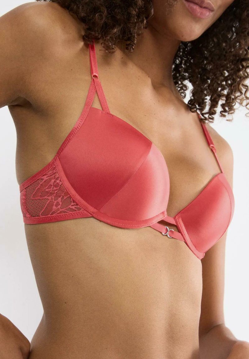 Soutien-gorge en satin rouge à finition lisse avec des panneaux latéraux en dentelle. Doté de bretelles réglables et d'un petit accent métallique au centre.