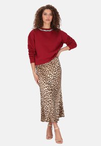 Sudadera roja con cuello decorativo, combinada con una falda de satén con estampado de leopardo, resaltada por una silueta ajustada y sandalias de tacón con tiras.