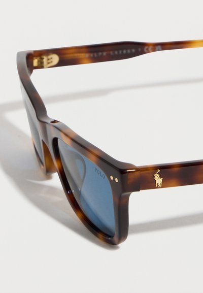 Ορθογώνια γυαλιά ηλίου σε σχέδιο χελώνας με μπλε φακούς, χρυσό λογότυπο Polo στο πλευρό και τοπογραφημένο το "POLO" στην γωνία του φακού.