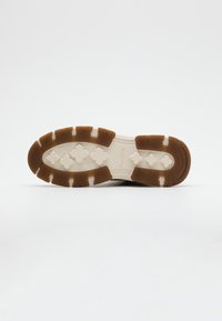 Suela de zapato en marrón y crema, con una superficie texturizada que presenta patrones en relieve y un diseño de agarre en zigzag para mayor tracción.