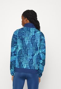 Blauw-gepatroneerde sportjas met abstracte ontwerpen, voorzien van een hoge kraag, elastische manchetten en een rekbare stof. Geweven accenten overal.