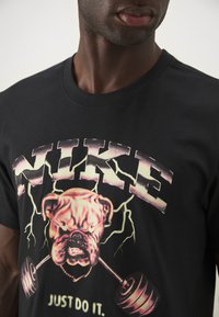 Sort bomulds t-shirt med et bulldog grafisk design, der løfter vægte, med teksten "NIKE" og "JUST DO IT" i fed, farverig skrift.