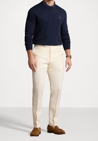 Marinblå stickad tröja med rund krage, krämfärgade linbyxor med skräddarsydd passform och bruna mockaloafers med tofsdetaljer.