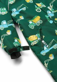Chaqueta impermeable verde con un patrón de camiones y vehículos de construcción en azul y amarillo. Incluye una cremallera y puños ajustables.