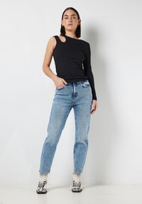 Zwarte geribbelde lange mouw top met een schouderuitsnede, gecombineerd met lichtblauwe rechte jeans en geprinte enklaarzen.
