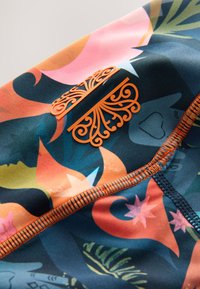 Maillot de bain arborant un motif vibrant et coloré avec des formes florales et abstraites en orange, rose et bleu. Comprend un détail logo texturé.