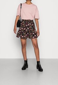 T-shirt rose à manches courtes associée à une mini jupe noire à motif floral. Bottines noires à talon épais avec des accents de fermeture éclair argentés.