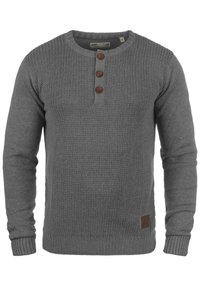 Maglione grigio lavorato a maglia con scollo rotondo, tre bottoni marroni al colletto e polsini e orlo a costine; dettaglio del tessuto testurizzato.