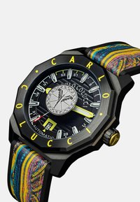 Automatische Uhr mit einem schwarzen achteckigen Gehäuse, gelben Akzenten und einem strukturierten mehrfarbigen Stoffarmband, das über ein auffälliges Logo und einen Datumsanzeiger verfügt.
