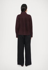 Jachetă din piele întoarsă burgundy, cu guler și mâneci lungi, combinată cu pantaloni negri largi. Materialul pare moale, cu o textură netedă.