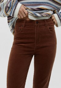 Bruine corduroybroek met een hoge taille, voorzien van zijzakken en een knoopsluiting, gecombineerd met een meerkleurige gestreepte trui.