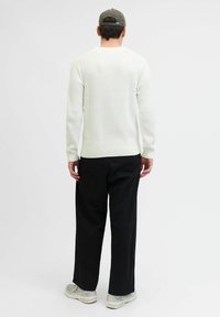 Maglione bianco a costine con maniche lunghe e scollo rotondo, abbinato a pantaloni neri a gamba larga e sneakers grigie. Vista dal retro.