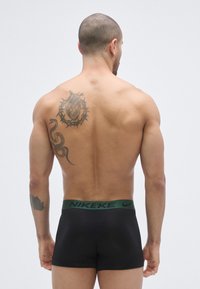 Sorte boxer briefs med en grøn Nike taljebånd, der har et tætsiddende design. En tatovering af et hjerte og en slange er synlig på ryggen.