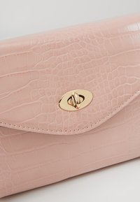 Pink faux leather clutch bag with a crocodile texture, featuring a gold-tone oval clasp and delicate stitching along the edges.