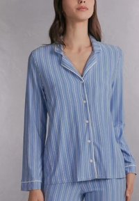 Blauw gestreept pyjamapakket gemaakt van zachte stof. Heeft lange mouwen, een knoopsluiting met een kraag en bijpassende broeken met een vergelijkbaar patroon.