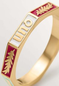 Anillo de oro con paneles de esmalte blanco y rojo, que presenta diseños de hojas de roble en relieve y la palabra "uno" en letras doradas sobre un fondo blanco.