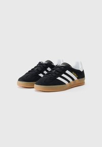 Sorte ruskinds sneakers med hvide striber og guld "Gazelle" branding. Har en gummisål og polstret tunge for komfort.