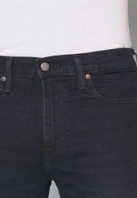 Jeans de mezclilla oscura con cierre de botón, diseño de cinco bolsillos y detalles de costura sutiles. Textura suave y ajuste ceñido.