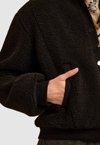 Giacca in pile nera con tessuto testurizzato, polsini a costine e una tasca anteriore, dotata di chiusura a bottoni e un design morbido e informale.
