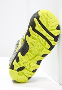 Sport shoe with a gray upper, yellow accents, and a textured black and yellow rubber sole. Features notable traction patterns.