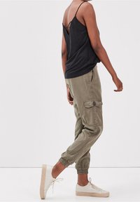 Black sleeveless top with a back detail, paired with olive green cargo pants featuring side pockets and cuffed hems, worn with light sneakers.