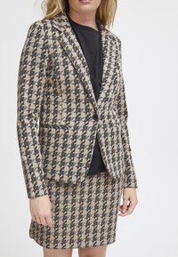 Béžová a černá houndstooth vzorová tweedová sako, s jedním knoflíkem, s klopami, v kombinaci s odpovídající sukní.
