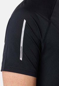 Zwarte sportshirt met korte mouwen, een slank ontwerp, meshtextuur en een wit logo en streepdetail op de linkerschouder.