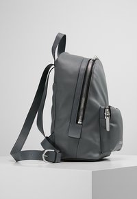 Sac à dos en cuir gris au design épuré, doté d'un grand compartiment principal zippé, d'une poche extérieure et de bretelles réglables.