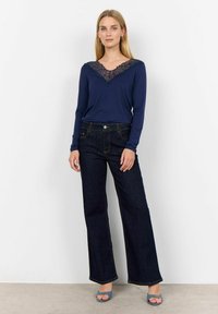 Mörkblå långärmad topp med spets V-urringning, i kombination med mörka vida jeans. Outfitten har ett mjukt material och en skräddarsydd passform.