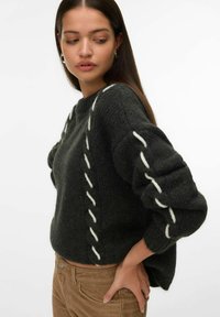 Maglione lavorato a maglia grigio scuro con dettagli di cucitura verticale bianchi, collo rotondo e maniche a palloncino oversize, abbinato a pantaloni in velluto a coste.