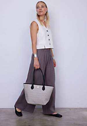 White sleeveless top with black buttons, gray wide-leg trousers, and a patterned tote bag with black handles. Smooth textures throughout.