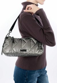 Bolso acolchado de color gris plata con un acabado brillante, que presenta acentos negros y una correa desmontable, llevado junto a un suéter de canalé.