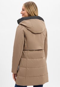 Beige pufferjas met een zwarte capuchon, voorzien van gestikte secties, lange mouwen en een verstelbaar koord in de taille.