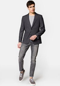 Szary żakiet o fakturowanym wykończeniu, z jednym guzikiem, w połączeniu z jasnoszarym t-shirtem, szarymi dżinsami i szarymi trampkami.