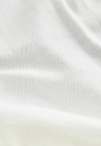 Nahaufnahme eines weichen, weißen Stoffes mit subtiler Webstruktur und sanften Falten.