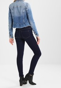 Jeansjacka i ljusblå, kort design med fransad nederkant. Mörka skinny jeans med slät yta, i kombination med svarta anklarstövlar.