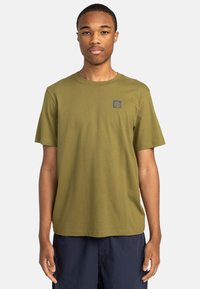Olivenfarbene Baumwoll-T-Shirt mit rundem Hals, kurzen Ärmeln und kleinem blauen Logo auf der linken Brust. Glatte Textur und lässige Passform.
