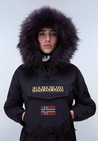 Svart huvajacka med lila pälsdetaljer, utrustad med en logotyp-patch och en Norges flagga-patch. Inkluderar en framficka och dragsko-detaljer.