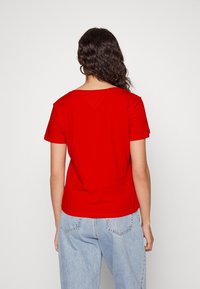 T-shirt rossa in cotone con scollatura arrotondata e maniche corte, caratterizzata da un leggero dettaglio a V sul retro e una vestibilità rilassata. Abbinata a jeans azzurri chiari.