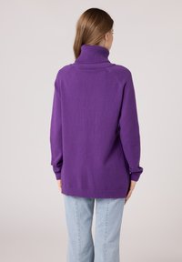 Maglione oversized viola con colletto alto, polsini e orlo a costine. Tessuto morbido con maniche raglan; fessure laterali nella parte inferiore.