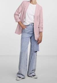 Světle růžový blazer přes bílý tričko, spárovaný se světle modrými rozšířenými džíny s vydřeným kolenem, doplněný černými teniskami.