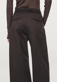 Zwarte wijde broek met een gladde, gestructureerde stof, elastische tailleband en twee achterzakken met knoopsluitingen.