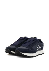 Un paio di sneakers basse di colore blu scuro con suola bianca e simboli bianchi su un lato, dotate di lacci blu navy e dettagli in camoscio.