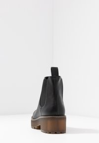 Czarny skórzany botek za kostkę z elastycznymi panelami po bokach i masywnym brązowym obcasem. Gładka faktura z pętelką z tyłu ułatwiającą zakładanie.
